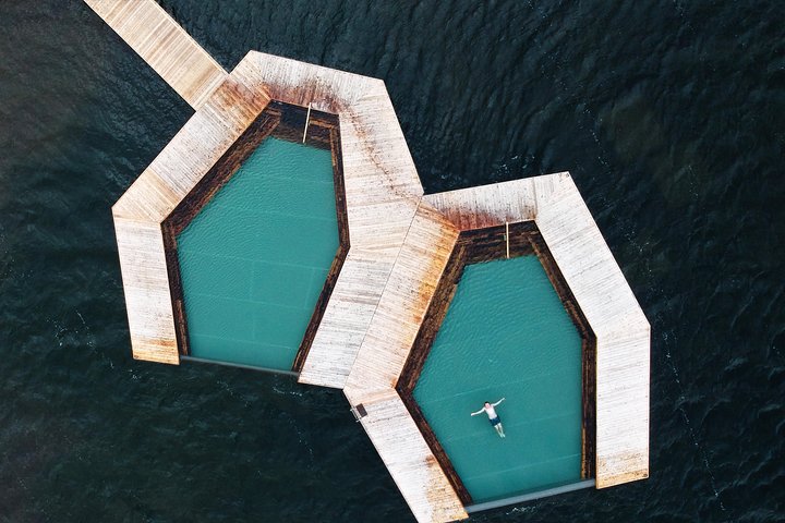 Aerial view of the Vök Baths in East Iceland, featuring two floating geothermal pools with a person relaxing in one, surrounded by the still waters of Lake Urriðavatn.