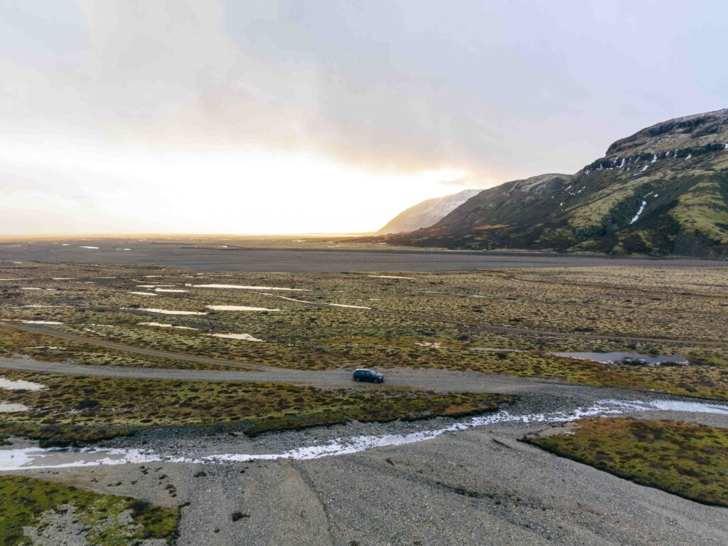 Car driving across gravel road in Icelandic highlands at sunset with mountains and rivers — Thrifty Car Rental Iceland self-drive adventure.